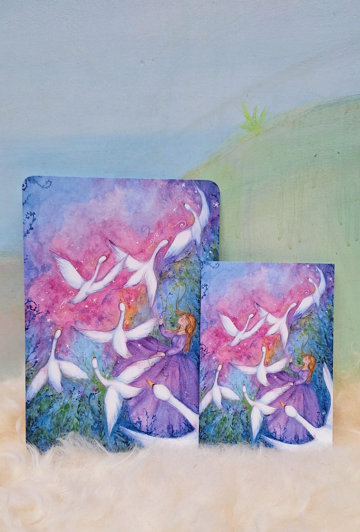 Postkarte Sieben Schwäne von Anne Gies A6 neben dem Kunstdruck A5 im Größenvergleich
