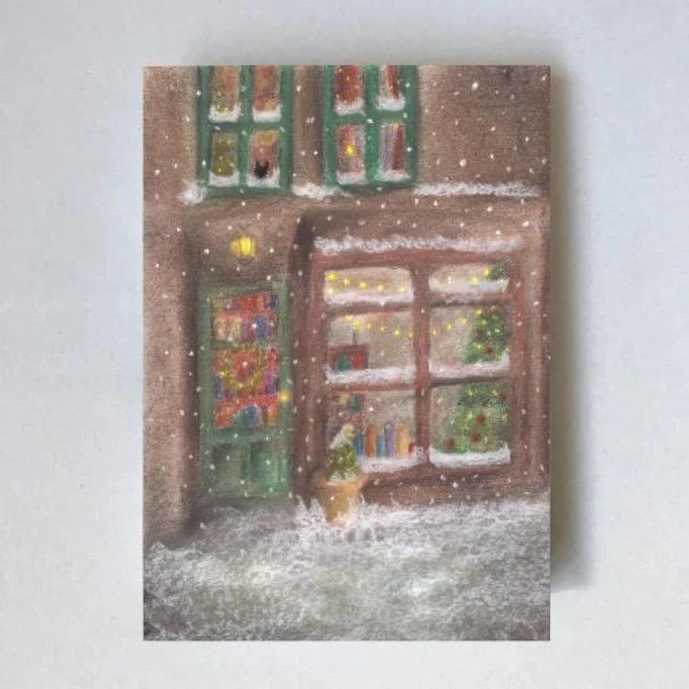 Postkarte Schaufenster von Lot Bouwes A6: ein weihnachtlich geschmücktes Schaufenster in einer verschneiten Straße, Kranz an der Tür, warmes Licht