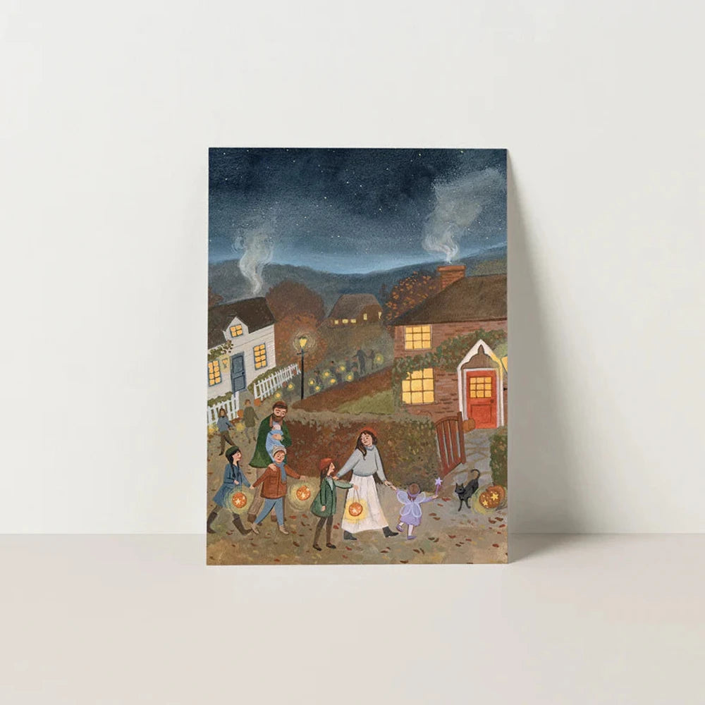 Postkarte Unten leuchten die Sterne von Robin Pieterse A6: Familien ziehen am Abend mit leuchtenden Kürbislaternen durch das Dorf, in den Häusern brennt Licht, aus den Schornsteinen steigt Rauch
