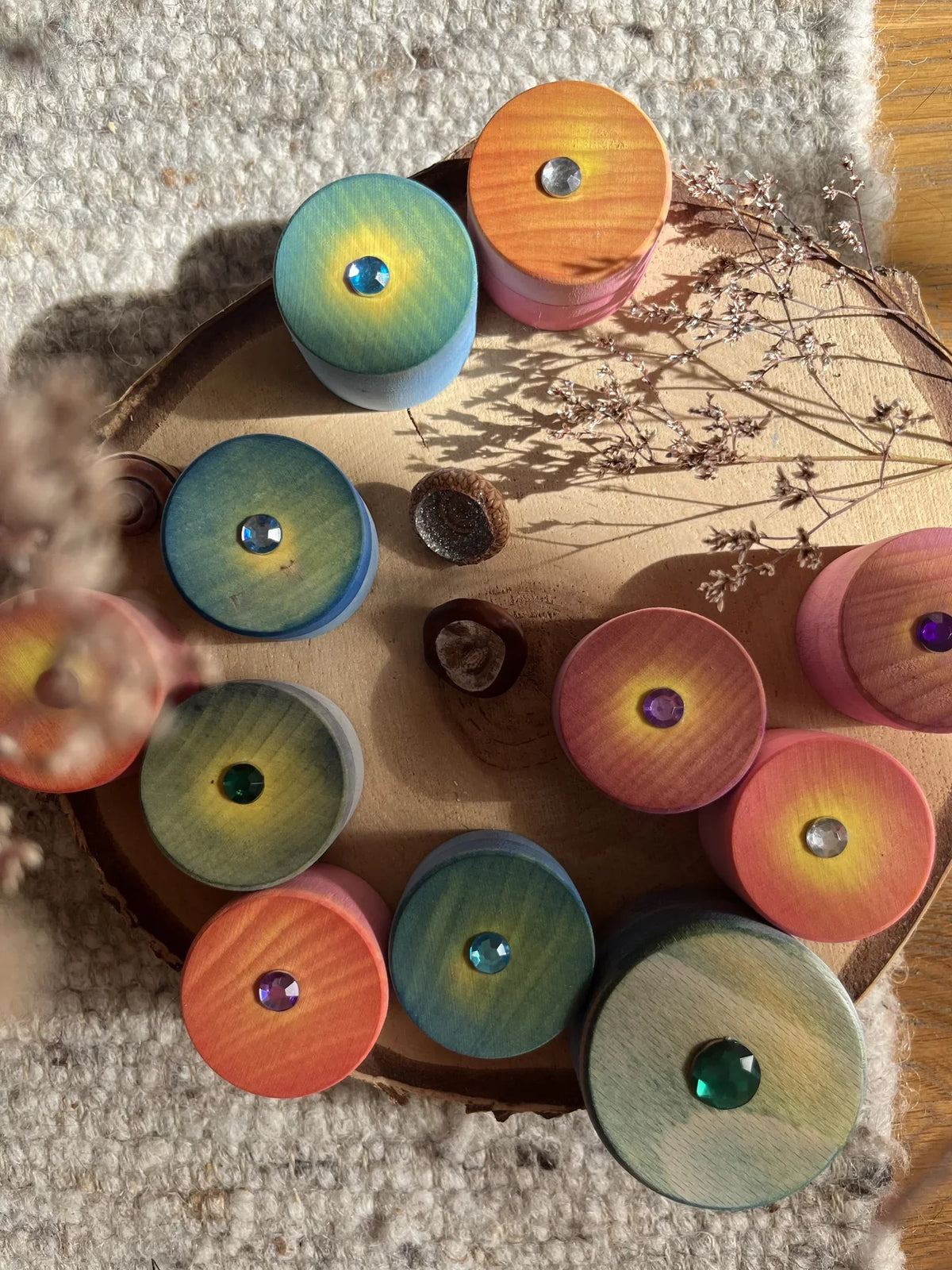Zauberdöschen aus Holz in vielen Farben, mit Aquarellfarbe bemalt, auf einer Baumscheibe