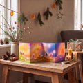 Adventskalender Baukje Exler, aufgestellter Kalender mit leuchtenden Farben auf einem Holztisch zwischen Kerzen und Tannenzweigen