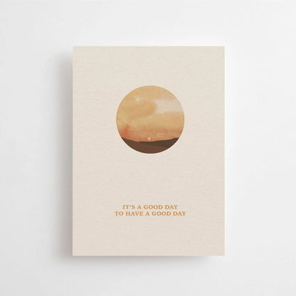 Postkarte A good day to have a good day von Anna Cosma A6: eine beige Karte mit einem Kreis, in dem ein Sonnenuntergang über dem Meer zu sehen ist, und dem Schriftzug „A good day to have a good day“