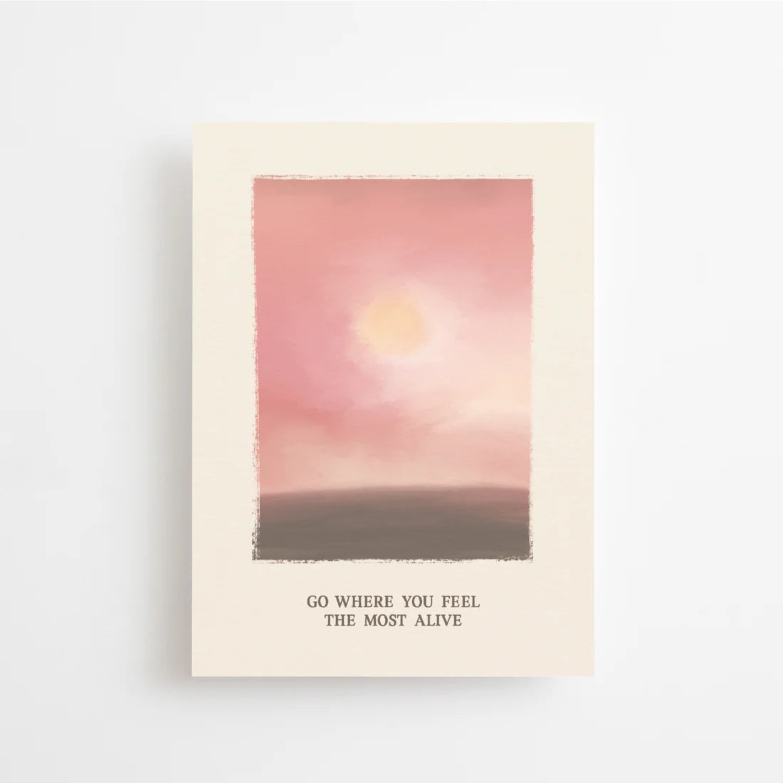 Postkarte Go where you feel the most alive von Anna Cosma A6: eine Karte mit gemaltem Abendhimmel in Rosé und Rot, einer tief stehenden Sonne über dunklem Land und dem Schriftzug „Go where you feel the most alive“