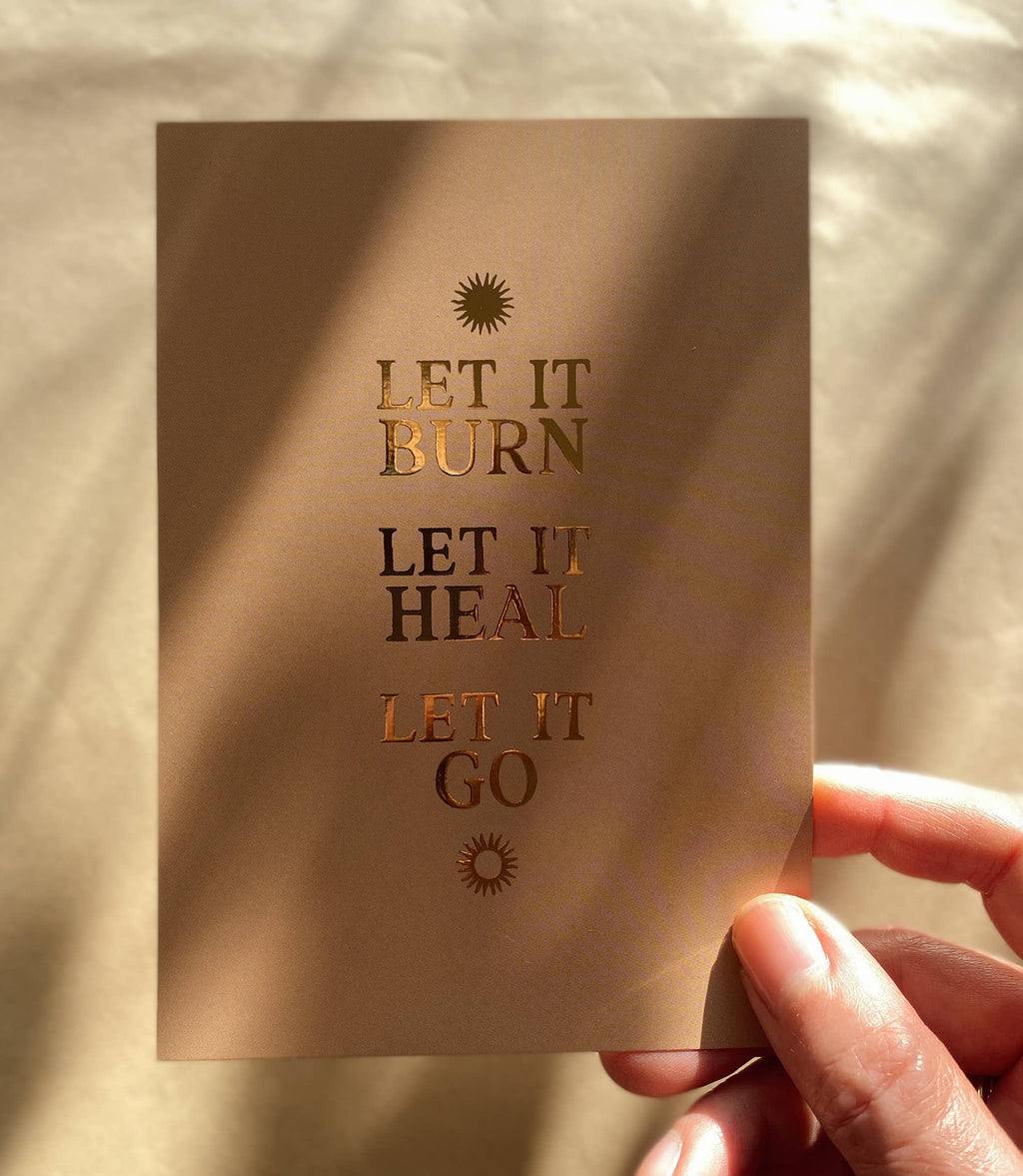Postkarte „Let it burn. Let it heal. Let it go.“ von Anna Cosma A6, in der Hand im Sonnenlicht