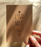 Postkarte „Let it burn. Let it heal. Let it go.“ von Anna Cosma A6, in der Hand im Sonnenlicht