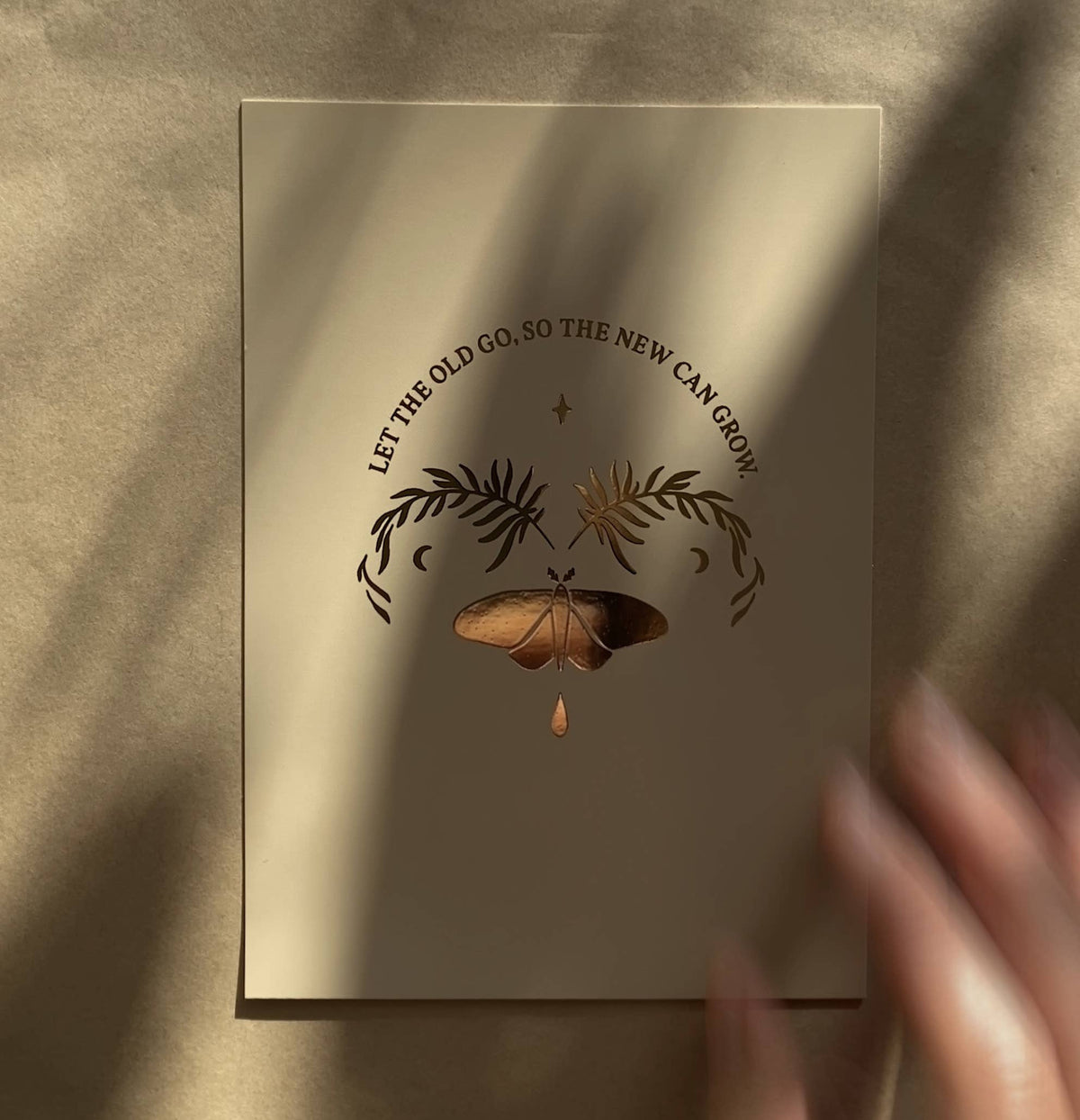 Postkarte „Let the old go, so the new can grow“ von Anna Cosma A6, in der Hand im Sonnenlicht