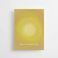 Postkarte „Make of yourself a light“ von Anna Cosma A6: eine gelbe Karte mit leuchtendem Sonnenkreis und dem Schriftzug „Make of yourself a light“