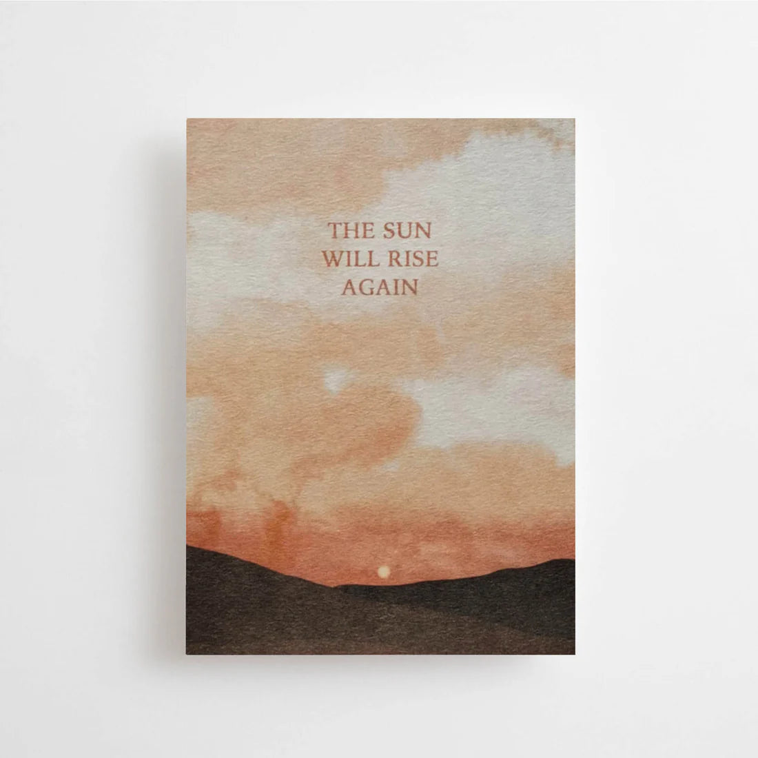 Postkarte The sun will rise again von Anna Cosma A6: eine Karte mit Himmel in Pfirsich und Orange über dunklen Hügeln und dem Schriftzug „The sun will rise again“