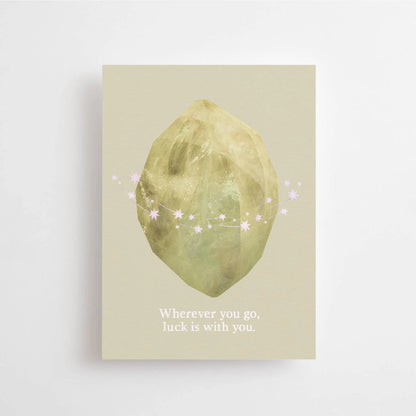 Postkarte Wherever you go, luck is with you von Anna Cosma A6: eine graugrüne Karte mit einer goldgrün schimmernden Form, kleinen Sternen und dem Schriftzug „Wherever you go, luck is with you“
