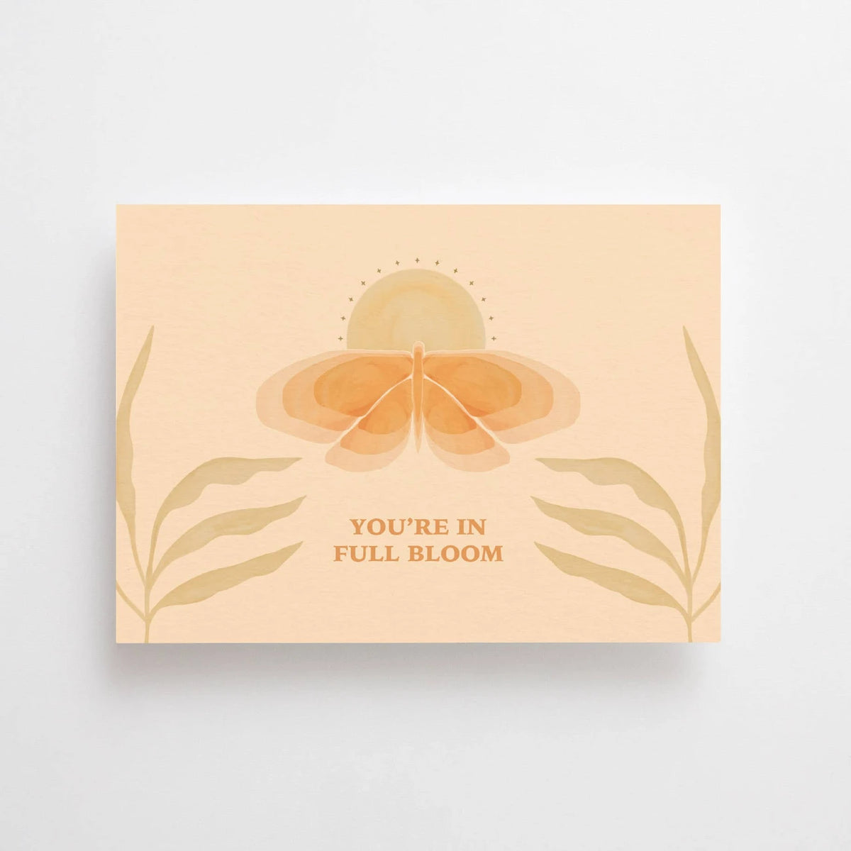 Postkarte You're in full bloom von Anna Cosma A6: eine pfirsichfarbene Karte im Querformat mit stilisierter Blüte zwischen Blättern und dem Schriftzug „You’re in full bloom“