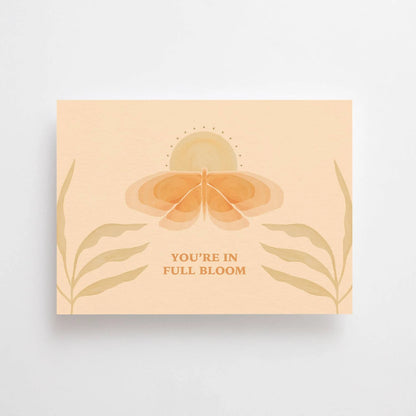 Postkarte You're in full bloom von Anna Cosma A6: eine pfirsichfarbene Karte im Querformat mit stilisierter Blüte zwischen Blättern und dem Schriftzug „You’re in full bloom“