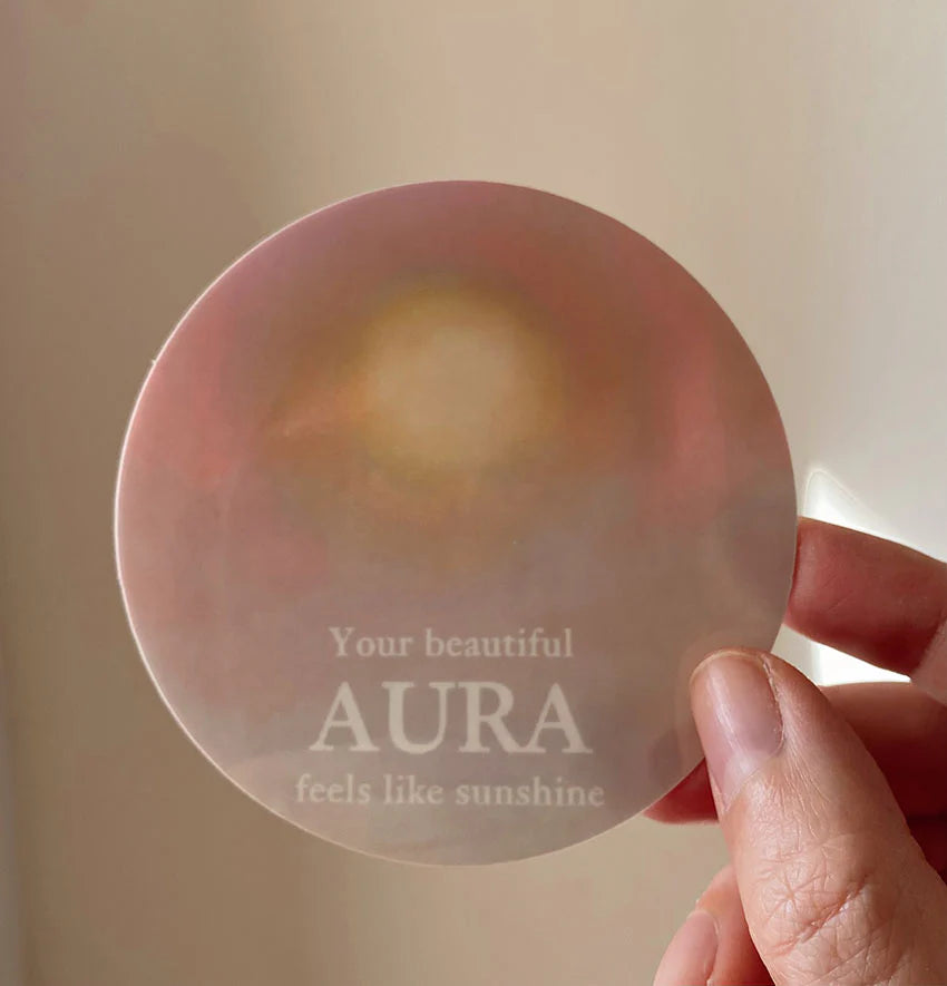 Vinyl-Sticker „Your beautiful aura feels like sunshine“ von Anna Cosma, in der Hand vor dem Licht