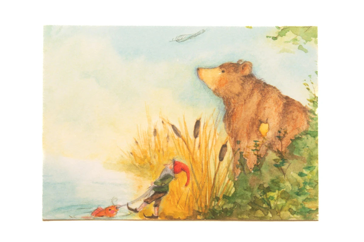 Postkarte Bär und Zwerg von Anne Gies A6: ein großer Bär schnuppert in den Wind, daneben zieht ein Zwerg mit roter Mütze am Seeufer zwischen Rohrkolben einen kleinen roten Fisch an der Leine