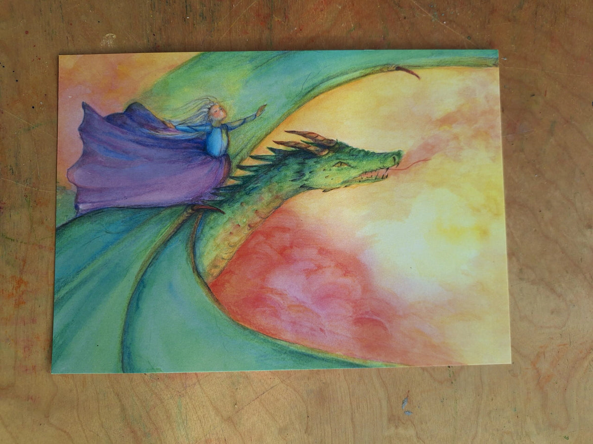 Postkarte Fliegender Drache von Anne Gies A6: eine Gestalt im violetten Umhang fliegt auf dem Rücken eines grünen Drachen durch einen Himmel in Rot, Gelb und Grün