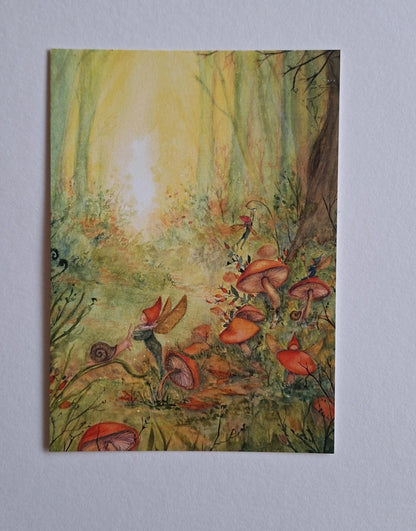 Postkarte Pixie von Anne Gies A6: ein kleiner Pixie mit spitzer Mütze sitzt zwischen orangen Pilzen im sonnigen Wald, daneben eine Schnecke