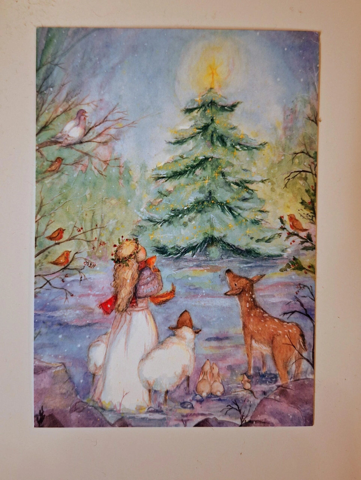 Postkarte Weihnachten von Anne Gies A6: Menschen und Tiere, darunter ein Schaf und ein Reh, versammeln sich im Schnee um einen geschmückten Tannenbaum mit leuchtendem Stern, ringsum kleine Vögel