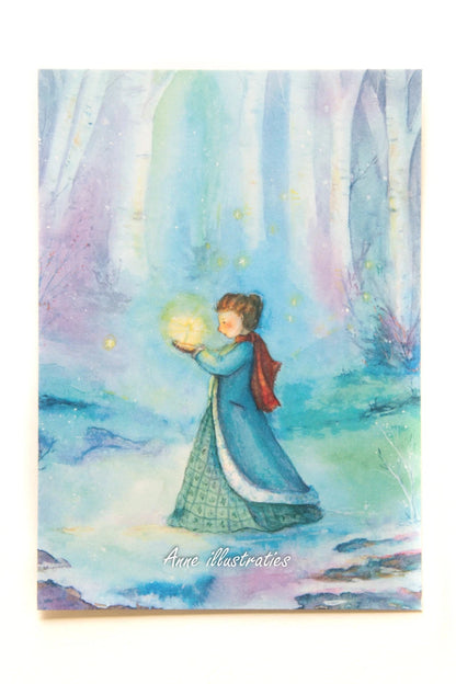Postkarte Winterelfe von Anne Gies A6: eine Gestalt im langen blauen Mantel mit rotem Schal hält ein leuchtendes Licht in einem nebligen blauen Winterwald