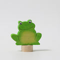 Grimm's Steckfigur Frosch, der grüne Frosch sitzt breit lächelnd auf seinem Holzfuß