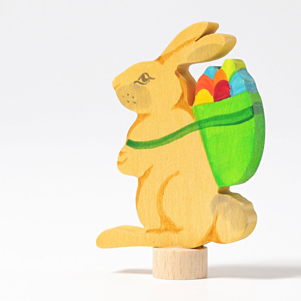 Grimm's Steckfigur Hase mit Korb, der gelbe Hase trägt einen grünen Korb voller bunter Eier auf dem Rücken