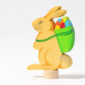Grimm's Steckfigur Hase mit Korb, der gelbe Hase trägt einen grünen Korb voller bunter Eier auf dem Rücken