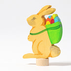 Grimm's Steckfigur Hase mit Korb, der gelbe Hase trägt einen grünen Korb voller bunter Eier auf dem Rücken
