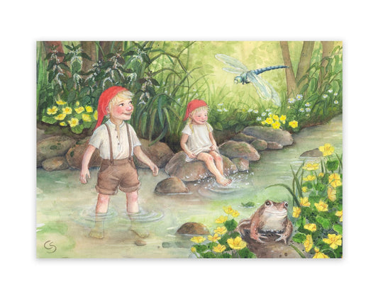 Postkarte Am Bach von Corinna Schwerdtfeger A6: zwei Wichtelkinder spielen barfuß im Bach zwischen gelben Sumpfdotterblumen, eine Libelle und ein Frosch schauen zu