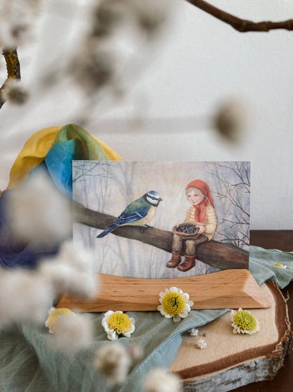 Postkarte Wichtel mit Blaumeise von Corinna Schwerdtfeger A6 auf einem Holzständer mit Blumen, Foto