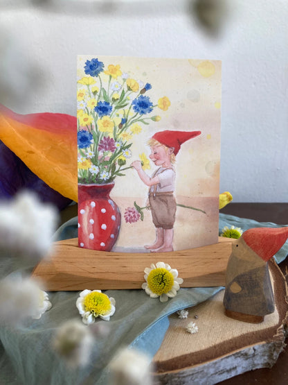 Postkarte Wichteljunge mit Sommerblumen von Corinna Schwerdtfeger A6 auf einem Holzständer mit Frühlingsblumen, Foto