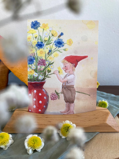 Postkarte Wichteljunge mit Sommerblumen von Corinna Schwerdtfeger A6 auf einem Holzständer mit Frühlingsblumen, Foto