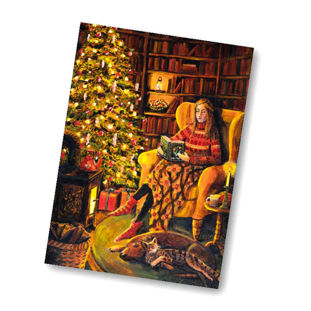 Postkarte Weihnachtswärme von Esther Bennink A6: eine Frau liest in einem Ohrensessel neben dem geschmückten Weihnachtsbaum, ringsum Geschenke und Bücher