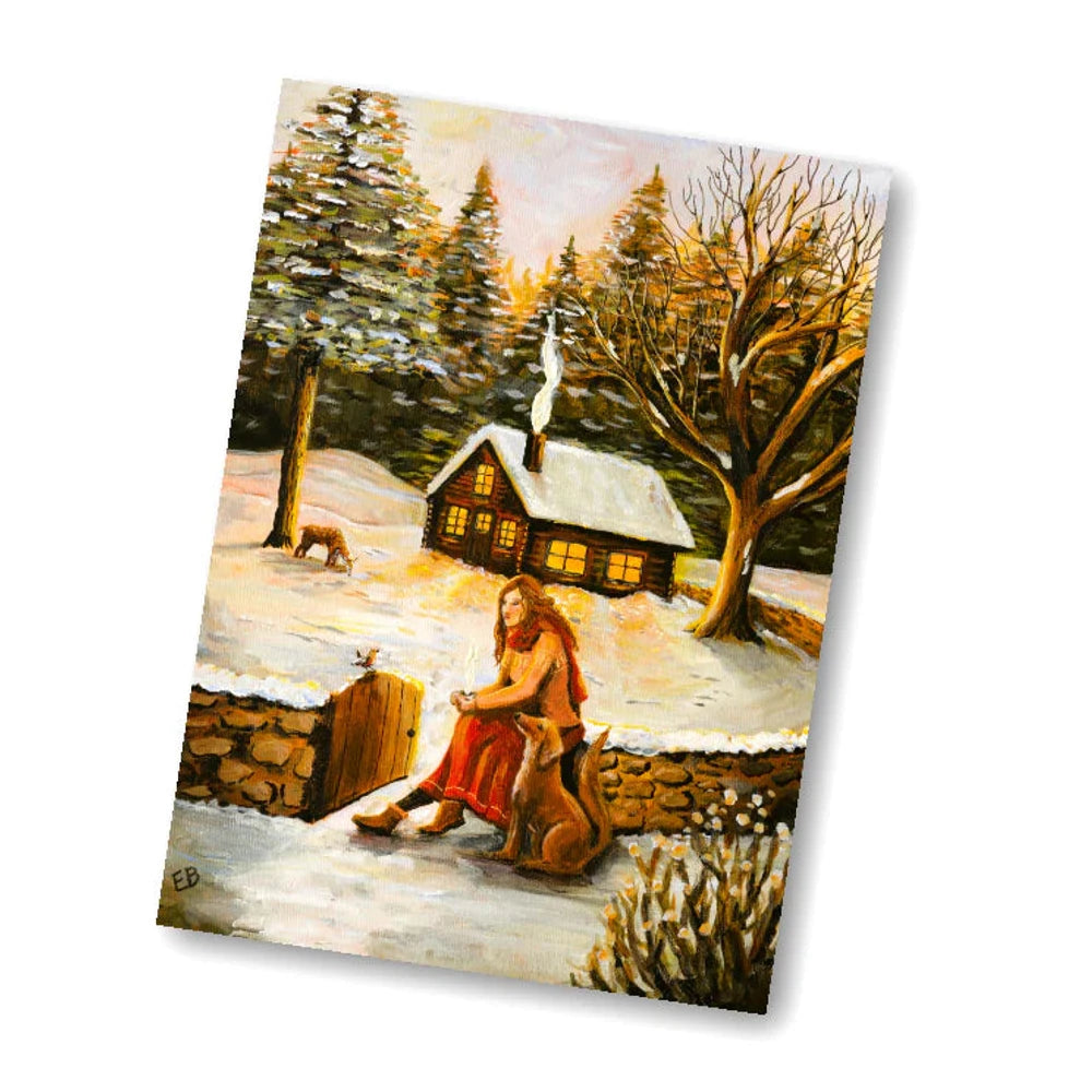 Postkarte Wintertag von Esther Bennink A6: eine Frau sitzt mit einer Tasse Tee vor einem verschneiten Häuschen zwischen Tannen