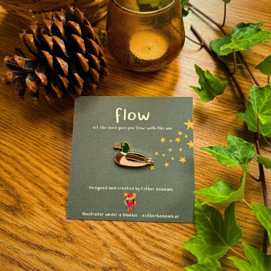 Emaille-Pin Ente flow von Esther Bennink, Emaille-Pin Ente auf einer dunklen Karte mit dem Spruch flow
