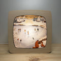 Motiv Winterspuren von Goose Grass Illustrations in der magischen Lampe, Familien beim Schlittschuhlaufen auf einem zugefrorenen See, zwei Füchse am Ufer