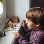Grapat Adventskalender 2026, Kind spielt mit Holzfiguren auf der Fensterbank