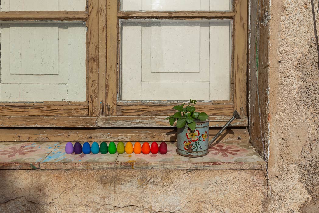Grapat Mandala Rainbow Eggs in einer Reihe auf einer Fensterbank vor einem Holzfenster