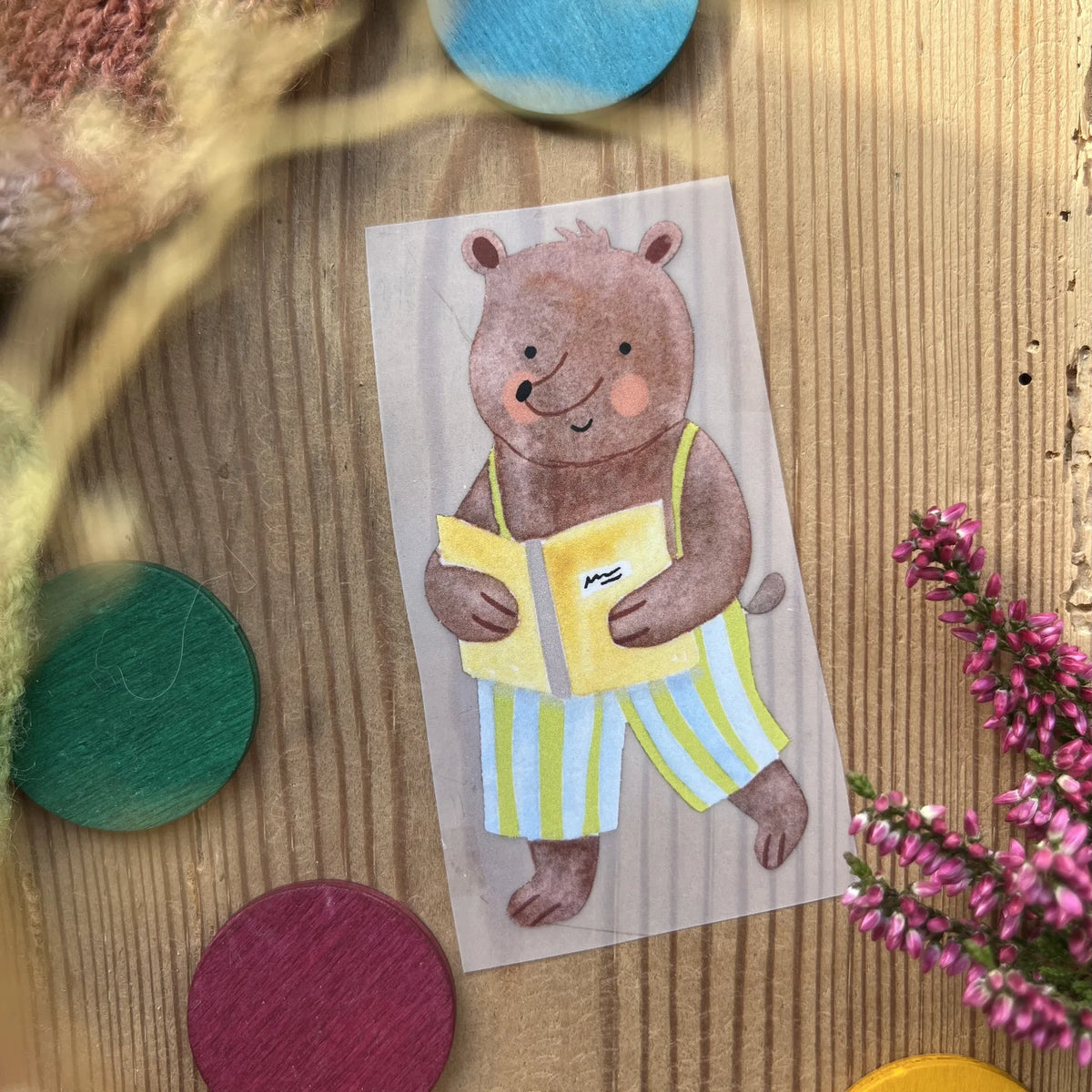 Hannahs Firlefanz Bügelbild Bär in Ringelhose mit Buch, auf Holz zwischen bunten Holzscheiben