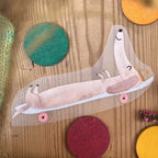 Hannahs Firlefanz Bügelbild Dackel, der lang ausgestreckt auf dem Skateboard liegt, auf Holz zwischen bunten Holzscheiben