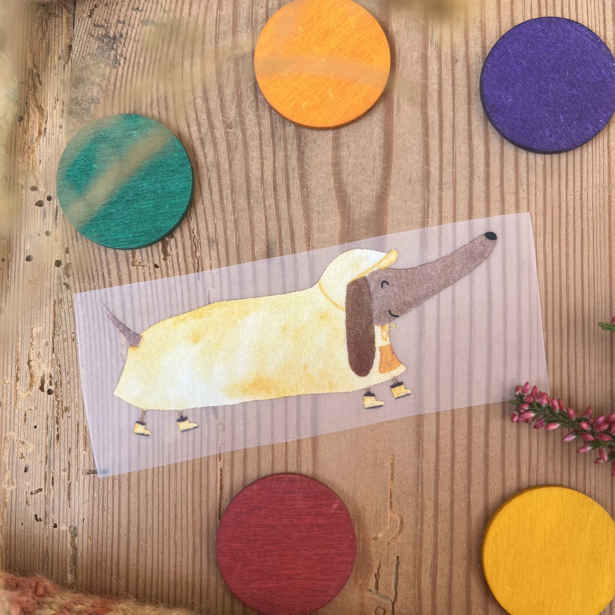 Hannahs Firlefanz Bügelbild Dackel im gelben Regenmantel, auf Holz zwischen bunten Holzscheiben