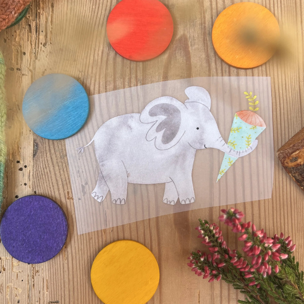 Hannahs Firlefanz Bügelbild grauer Elefant mit Schultüte im Rüssel, auf Holz zwischen bunten Holzscheiben