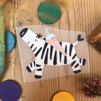 Hannahs Firlefanz Bügelbild springendes Zebra mit Schultüte, auf Holz zwischen bunten Holzscheiben