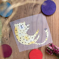 Hannahs Firlefanz Bügelbild verspielter Gepard auf dem Rücken, auf Holz zwischen bunten Holzscheiben