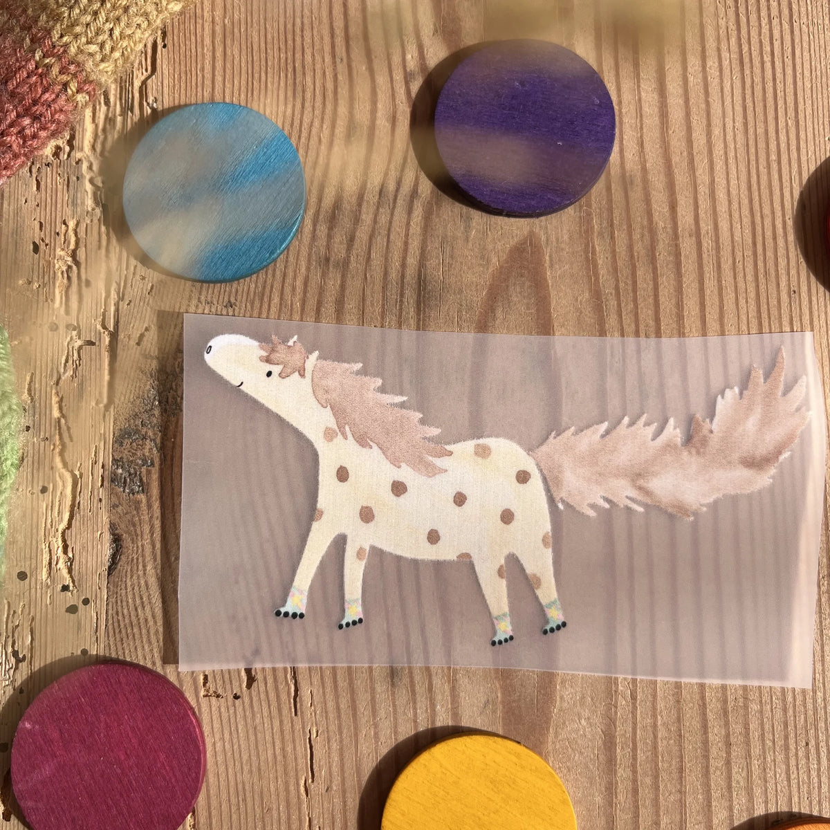 Hannahs Firlefanz Bügelbild geflecktes Pony mit langem Schweif, auf Holz zwischen bunten Holzscheiben