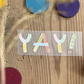 Hannahs Firlefanz Bügelbild Schriftzug Yay! in bunten Buchstaben, auf Holz zwischen bunten Holzscheiben