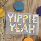 Hannahs Firlefanz Bügelbild Schriftzug Yippie Yeah in bunten Buchstaben, auf Holz zwischen bunten Holzscheiben