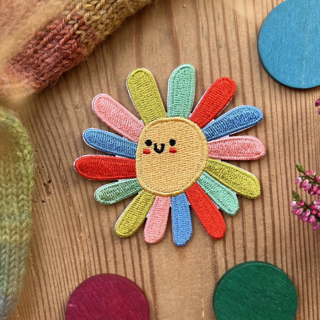 Hannahs Firlefanz Patch lachende Blume mit bunten Blütenblättern, gestickt, auf Holz zwischen bunten Holzscheiben