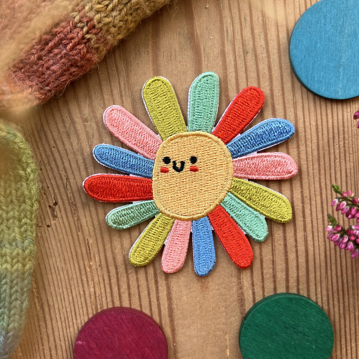 Hannahs Firlefanz Patch lachende Blume mit bunten Blütenblättern, gestickt, auf Holz zwischen bunten Holzscheiben