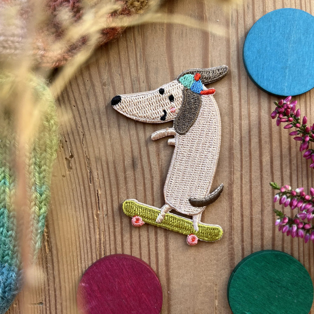 Hannahs Firlefanz Patch Dackel mit Cap auf dem Skateboard, gestickt, auf Holz zwischen bunten Holzscheiben