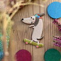 Hannahs Firlefanz Patch Dackel mit Cap auf dem Skateboard, gestickt, auf Holz zwischen bunten Holzscheiben