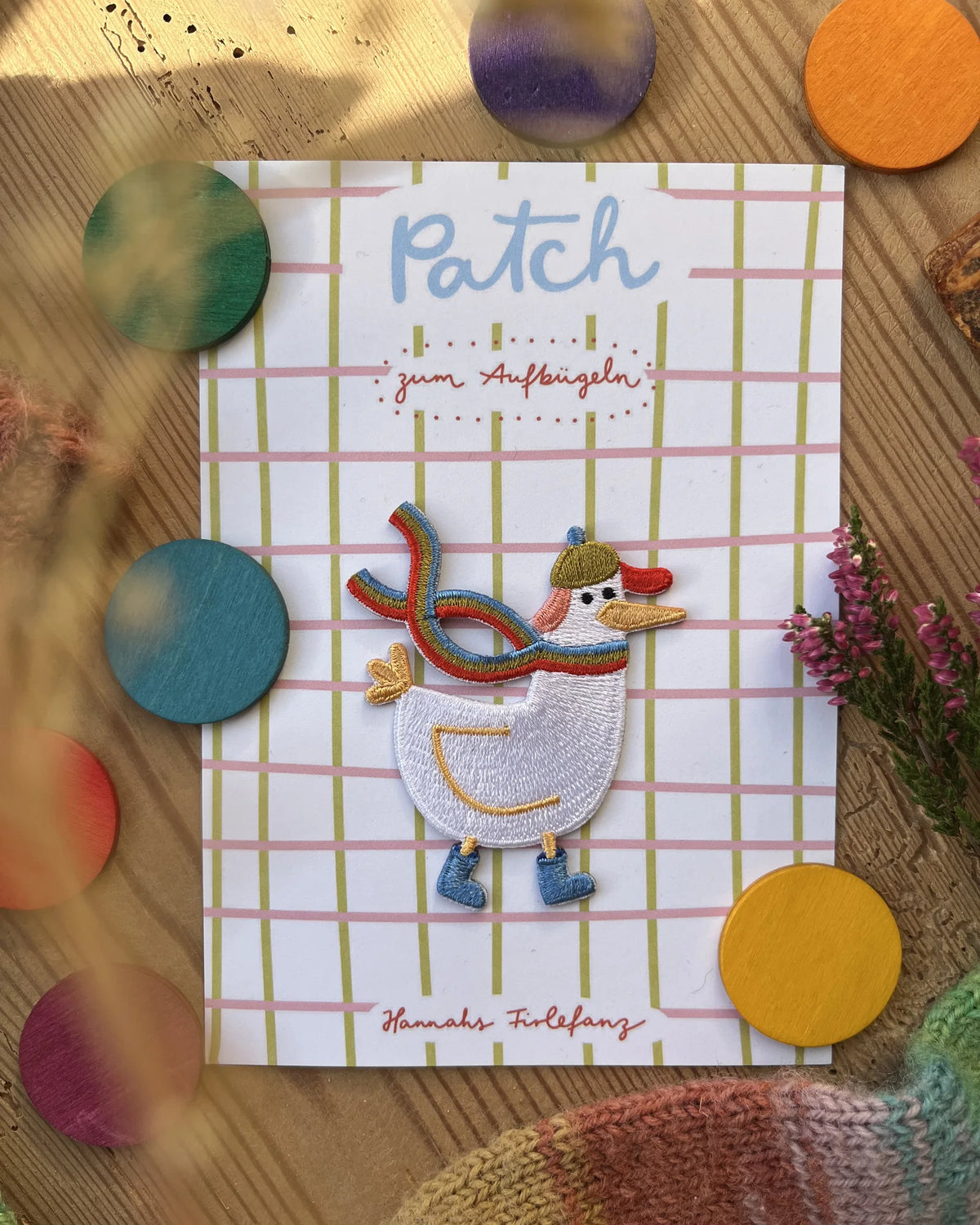 Hannahs Firlefanz Patch Gans mit Regenbogenschal und Mütze, auf der karierten Karte Patch zum Aufbügeln