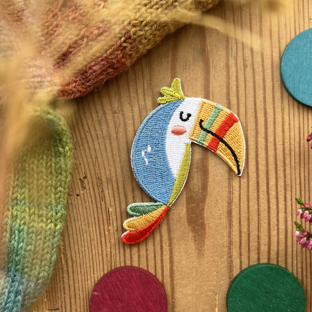 Hannahs Firlefanz Patch Tukan mit Regenbogenschnabel, gestickt, auf Holz zwischen bunten Holzscheiben